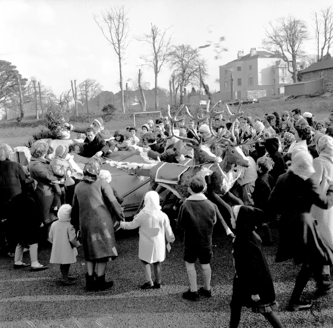 Father Christmas meets the local children with some presents on the Beau Sejour hard playing surface in 1964. what is now the Sports Commission base is the building on the right and beyond the lopped trees in the background is high netting on the tennis court perimeter