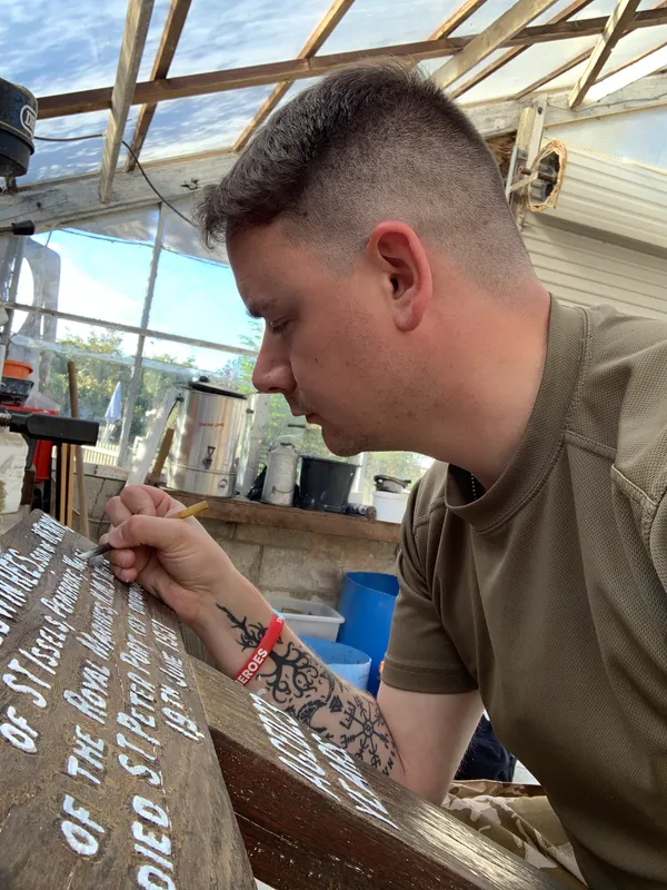 Matt Hill, a sergeant with the Guernsey Royal Marines Cadets, who says he has the marine corps in his blood, repainting the inscription on the cross. 