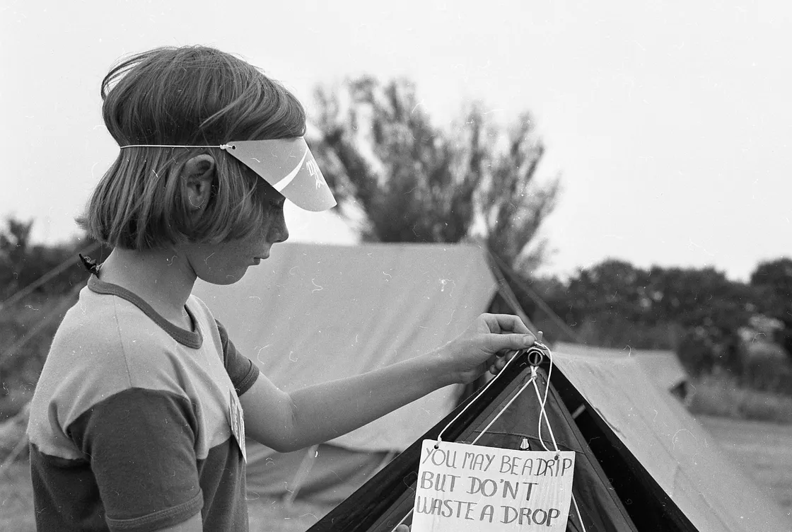 Anthony (now known as Tony) Bott, of the 2nd Guernsey Eagles, hangs a drought-themed sign on his tent during a cooking and camping competition at Rue Maingy, which was sponsored by the Coca-Cola Company.