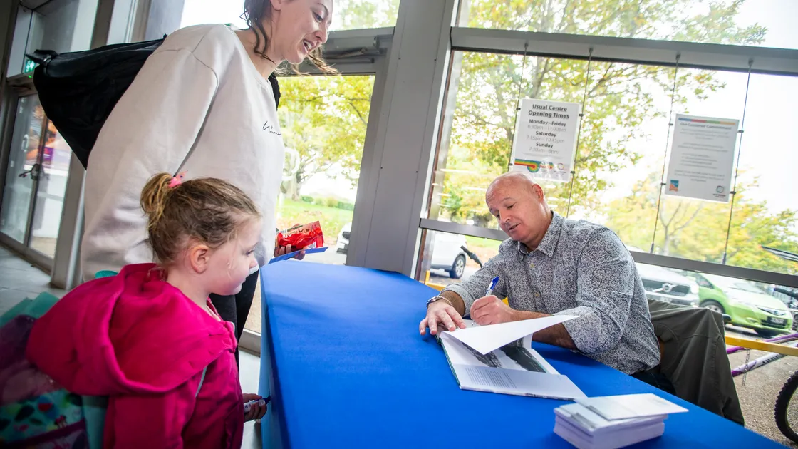 Marco Tersigni signing a copy of his book, Guernsey Past & Present – From The Exact Spot’ for Josie Dorey, who was with three-year-old Olivia Jones. (Picture by Luke Le Prevost, 31445721)