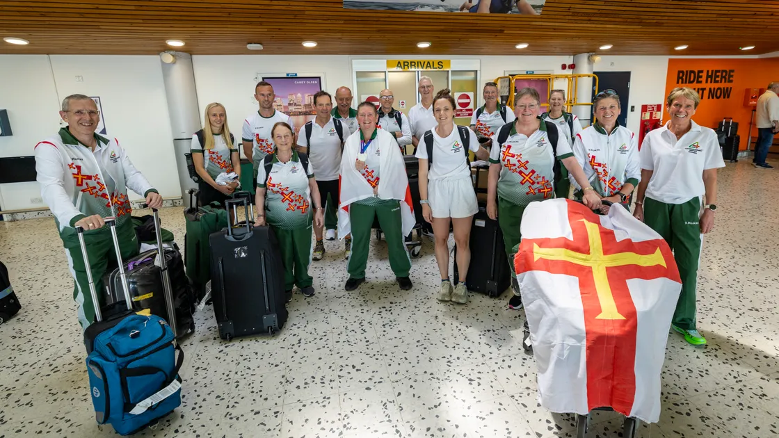 The remaining athletes, management team and supporters arrived back to Guernsey today after their time at the Commonwealth Games in Glasgow with some extra special luggage on board, the silver medal belonging to bowler Alison Merrien (centre).