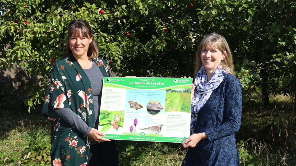 Brooke Kenyon, right, managing director of Orchard PR, and Donna Francis, president of La Societe Guernesiaise, holding the information board which the company has sponsored for Le Jardin de Lorette, the orchard and nature reserve in the Capelles.