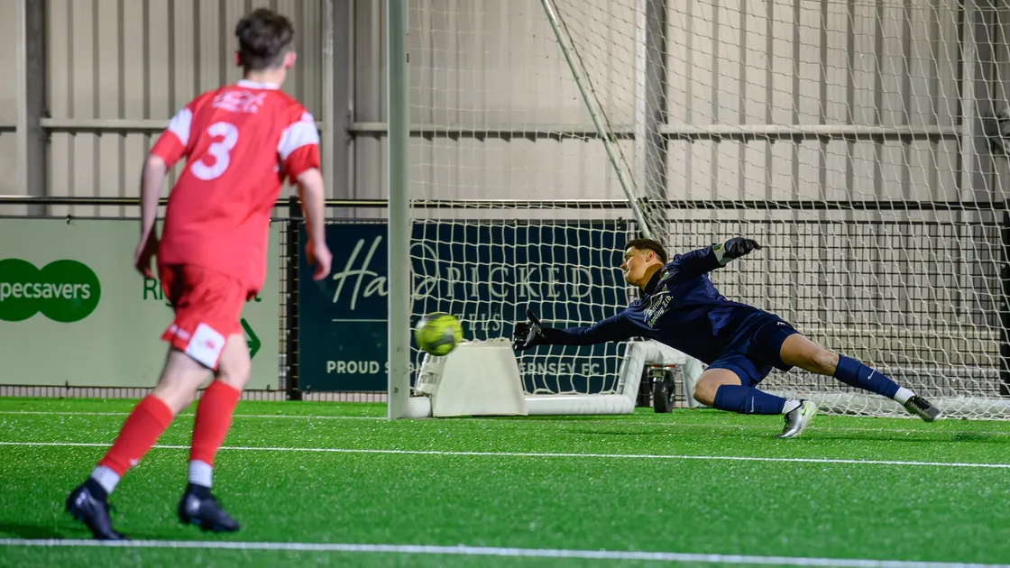 Sylvans goalkeeper Nick Batiste goes the right way but is unable to reach Louis Hunter's penalty