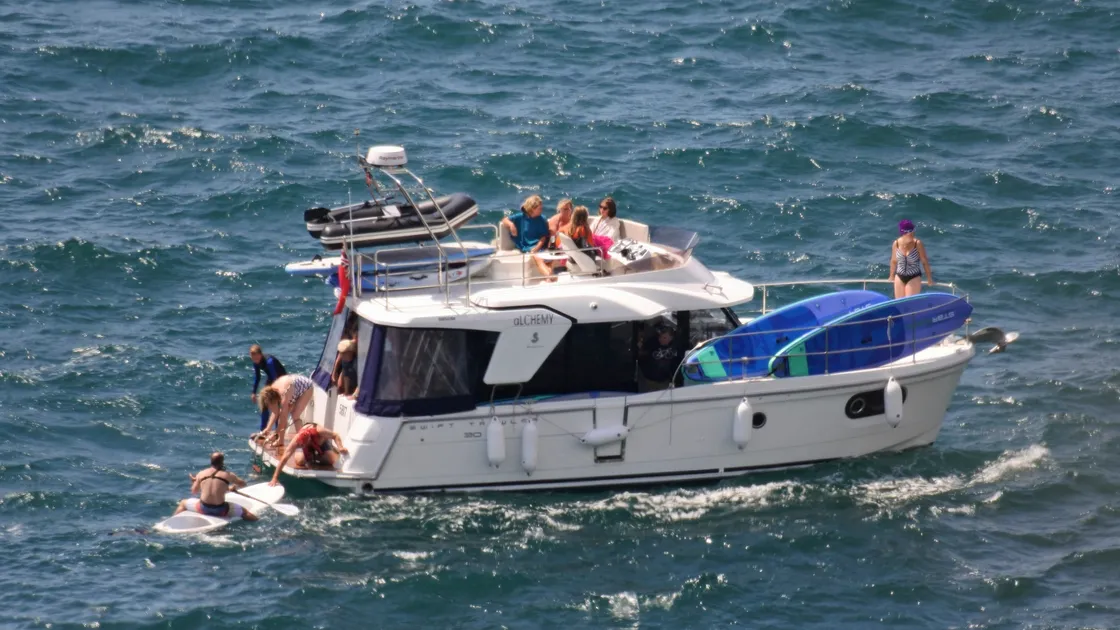 A passing motorcruiser picks up the last of a group of struggling paddleboarders just south of Icart Point on Sunday afternoon. (25383023)