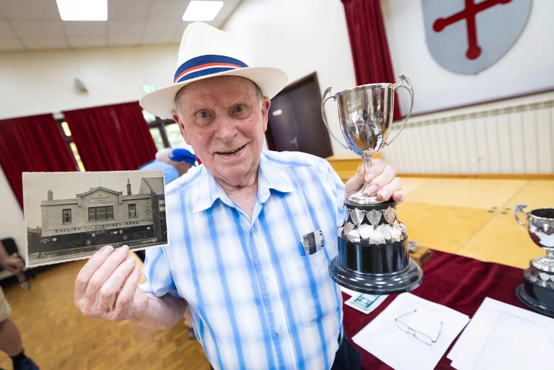 John Benham with the Benham Cup which was donated to the regatta by his father. He is pictured with a photograph of himself peering through the window of the flat above the E&G in the 1930s.