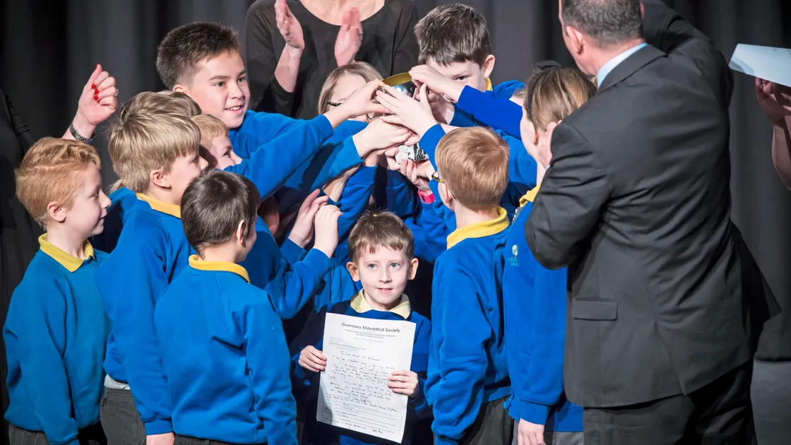 Picture By Peter Frankland. 08-03-19 Eisteddfod Class 1216 - Adjudicator Steven Roberts passes the trophy to the Le Rondin Primary School Choir. (24080887)