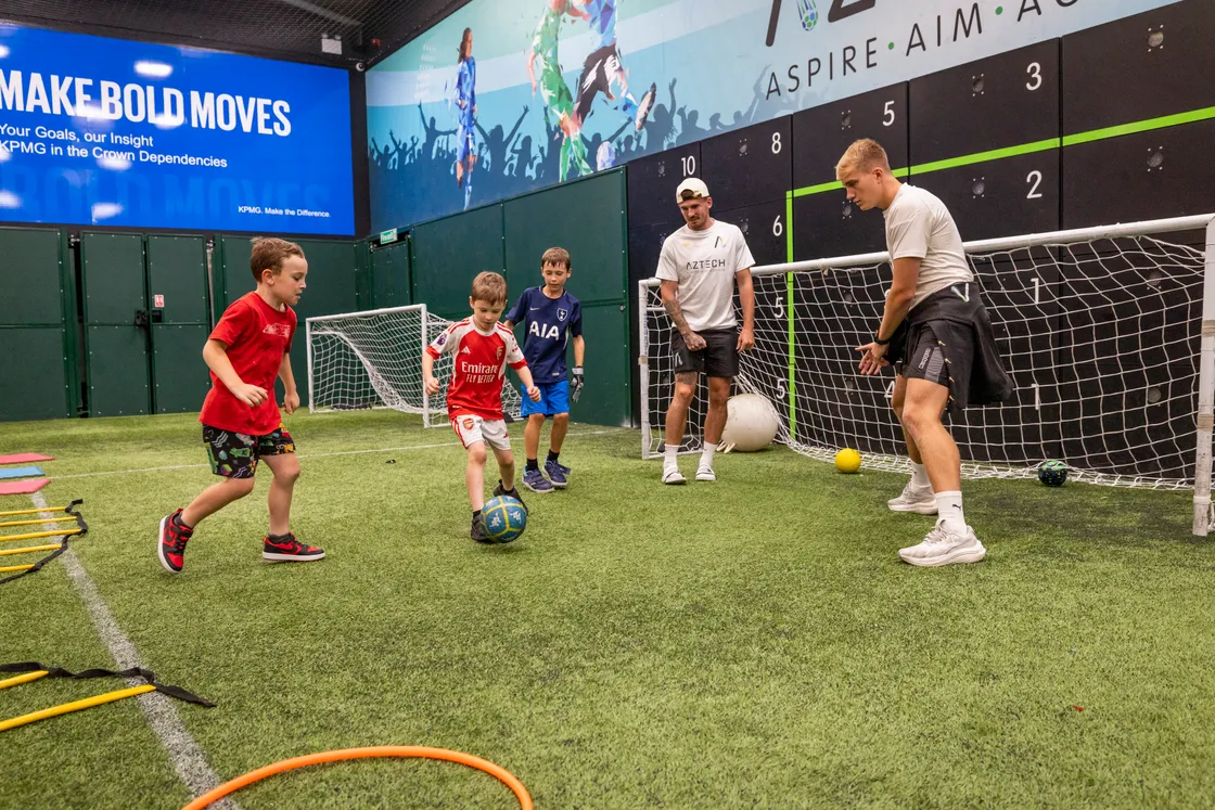 Billy Lewis, 7, Ethan Mullaly, 8, and Edward Greenway, 6, playing football with Aztech coaches Charlton Gauvain and Frazer Maginnis.