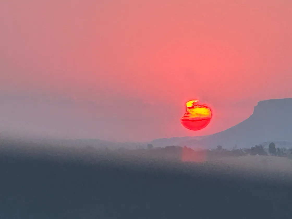 An almost full and partly clouded sun sets, as seen through a tinted car windscreen. 